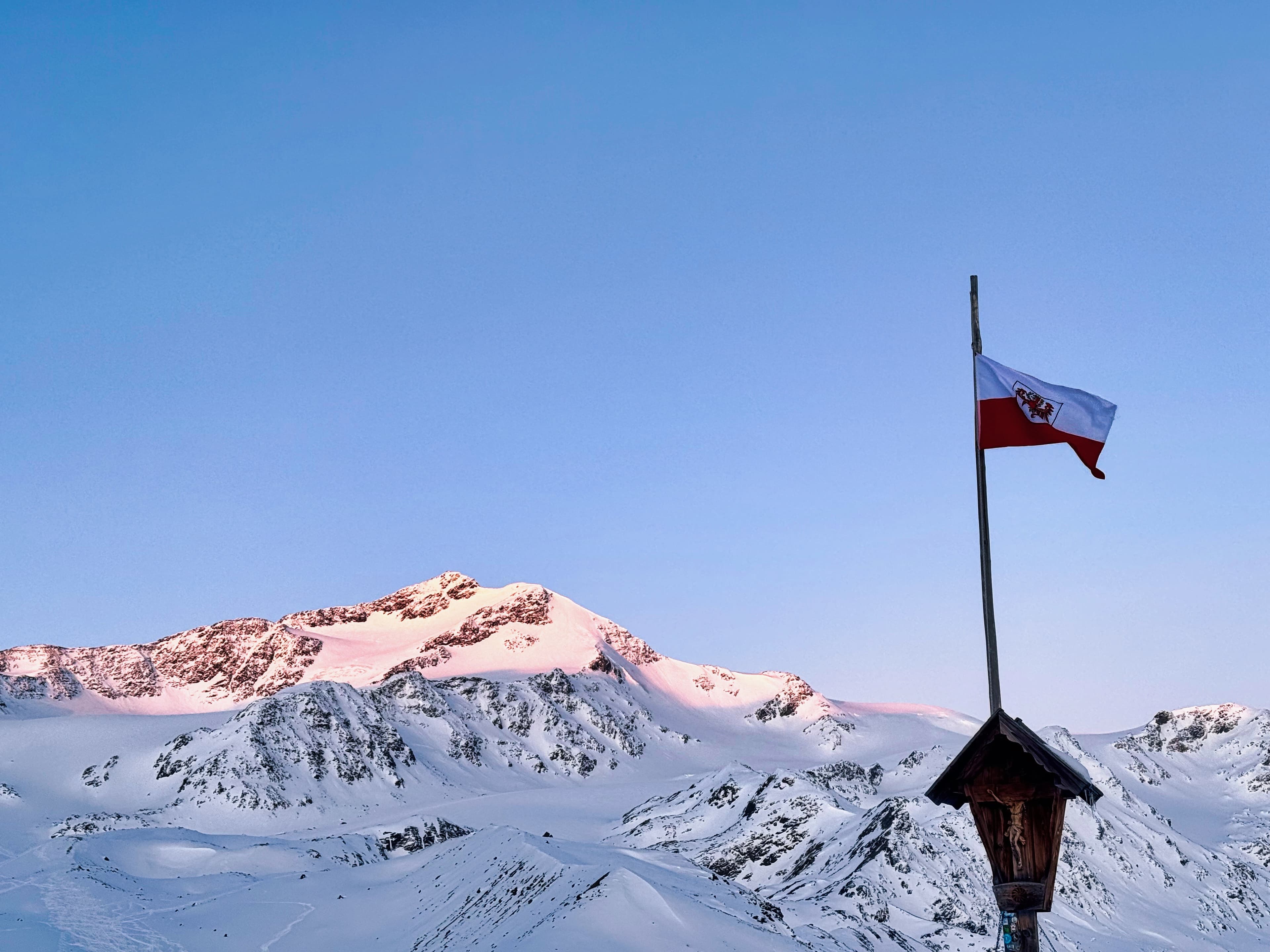 Alpenglow on an Ortler peak at dawn with Austrian flag