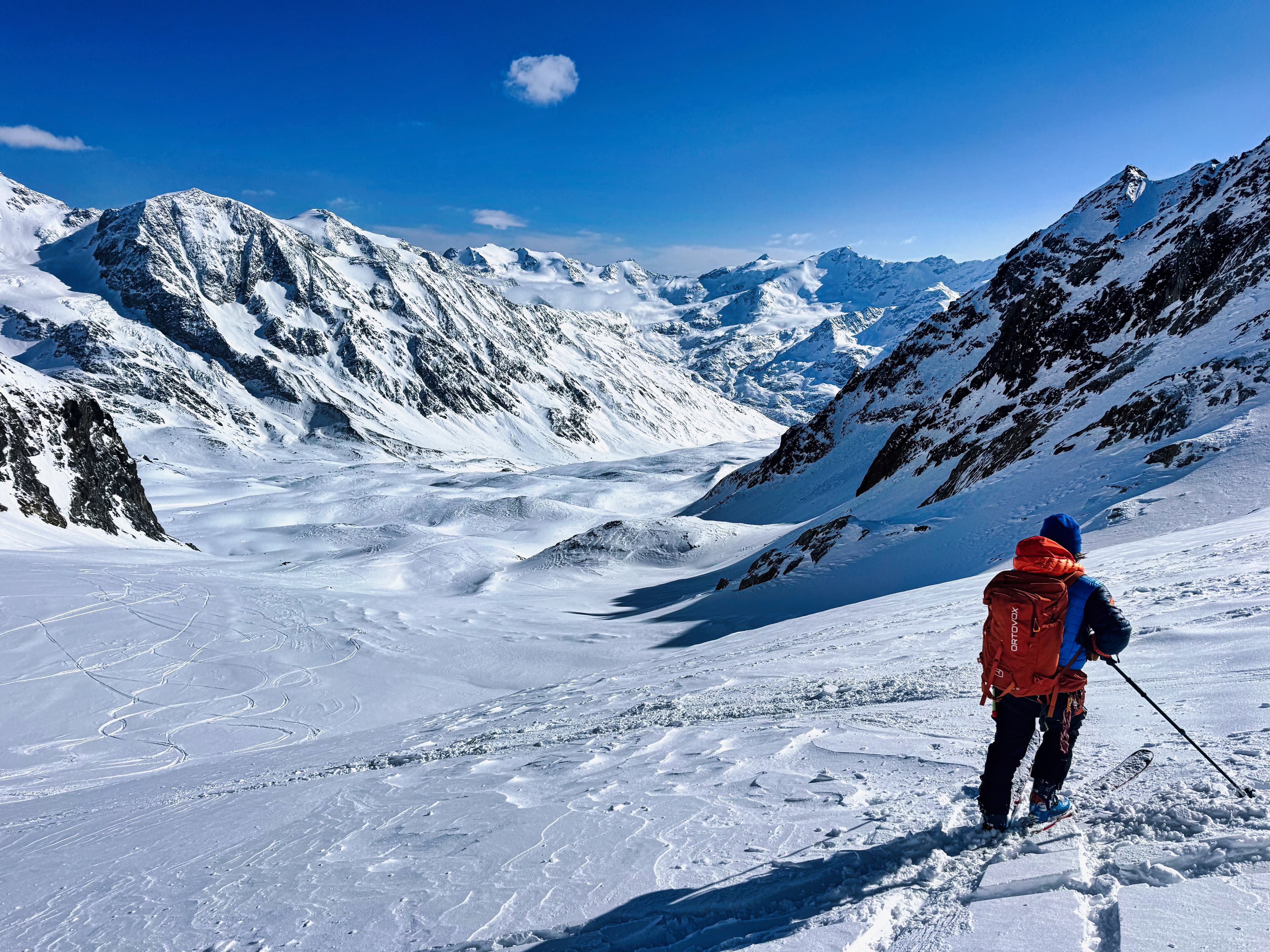 Skier with red pack overlooking a vast glacier valley in the Ortler Alps, bluebird sky