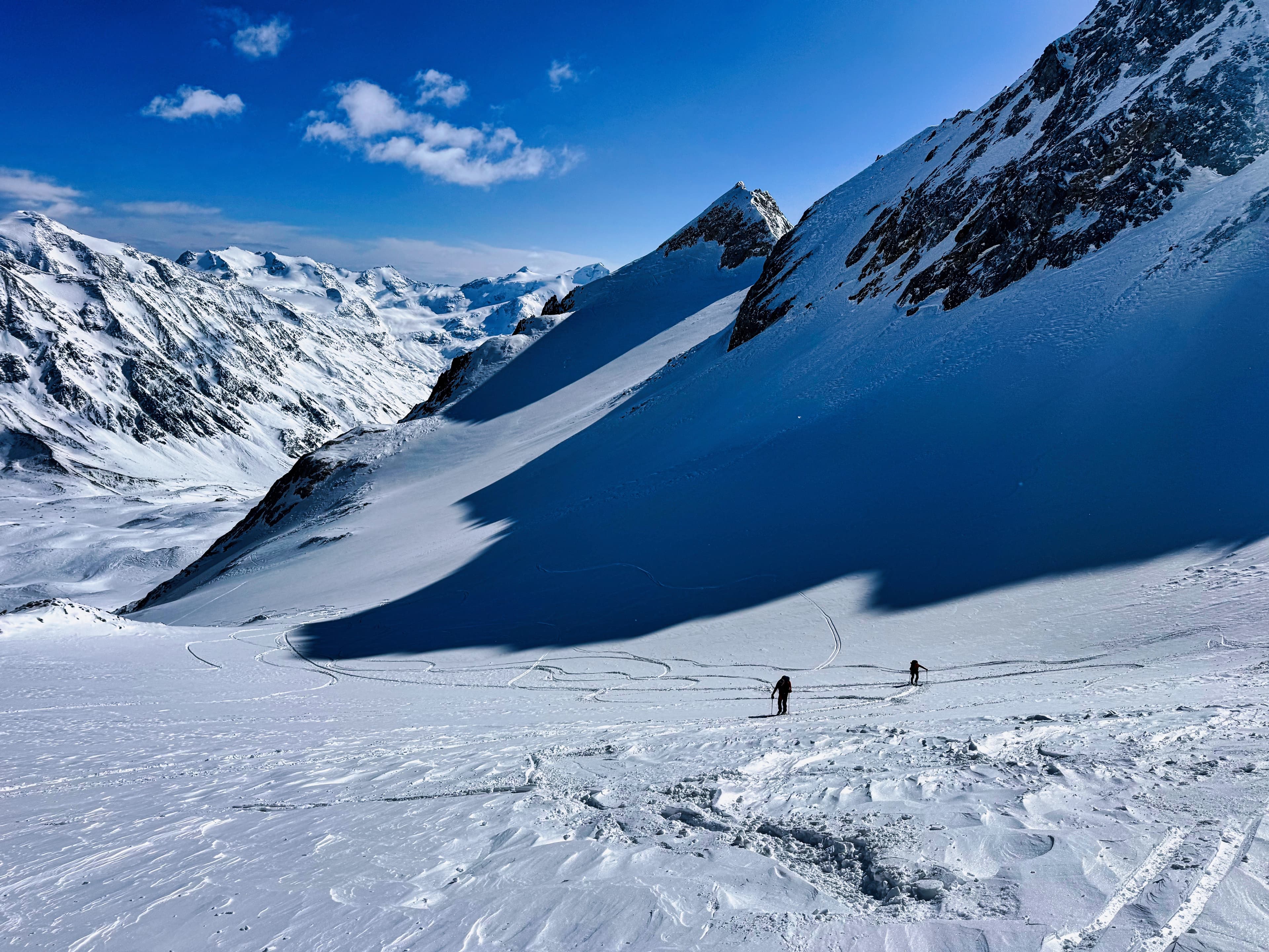 Two skiers crossing a glacier beneath dramatic mountain shadows